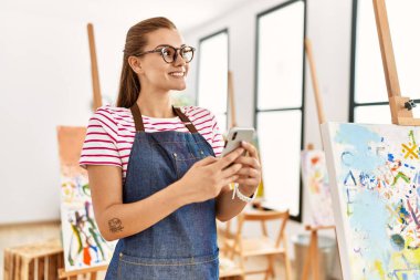Sanat stüdyosunda akıllı telefon kullanan kendine güvenen genç bir kadın.