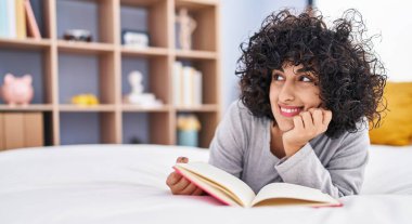 Young middle east woman reading book lying on bed at bedroom