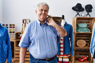 Perakende dükkanında elinde alışveriş poşetleri tutan yaşlı adam pozitif ve mutlu görünüyor ve kendine güvenen bir gülümsemeyle dişlerini gösteriyor. 