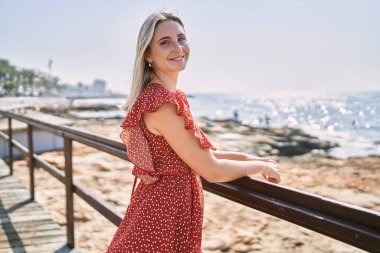 Kumsalda mutlu mutlu gülümseyen genç sarışın kız.