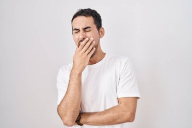 Handsome hispanic man standing over white background bored yawning tired covering mouth with hand. restless and sleepiness. 