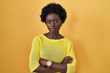 African young woman standing over yellow studio skeptic and nervous, disapproving expression on face with crossed arms. negative person. 