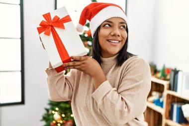 Hispanic brunette woman holding christmas present at home