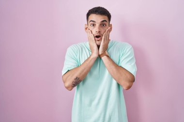 Yakışıklı İspanyol adam pembe arka planda duruyor. Korkmuş ve şok olmuş, şaşırmış ve şaşırmış. 