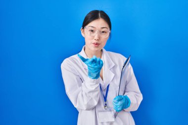 Laboratuvarda çalışan Çinli genç bir kadın kameraya bakıp havada bir öpücük savuruyor ve sevimli ve seksi oluyor. aşk ifadesi. 