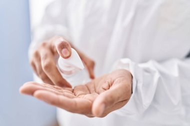 Young hispanic man pouring sanitizer gel on hand at laboratory
