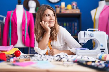 Young woman tailor smiling confident sitting on table at sewing studio
