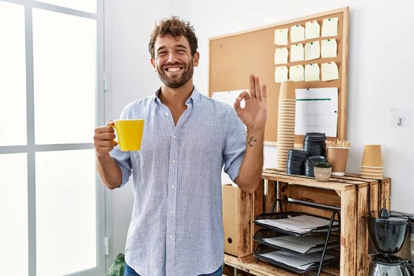 Genç Yakışıklı Adam Ofiste Kahve Içiyor Parmaklarıyla Imza Atıyor Gülümseyerek — Stok fotoğraf