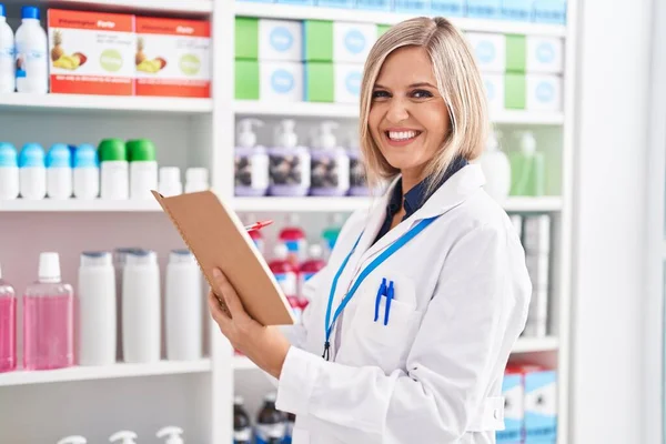 Young Blonde Woman Pharmacist Smiling Confident Reading Notebook Pharmacy — Foto de Stock