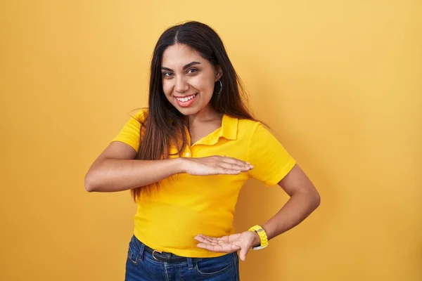 Young arab woman standing over yellow background gesturing with hands showing big and large size sign, measure symbol. smiling looking at the camera. measuring concept.