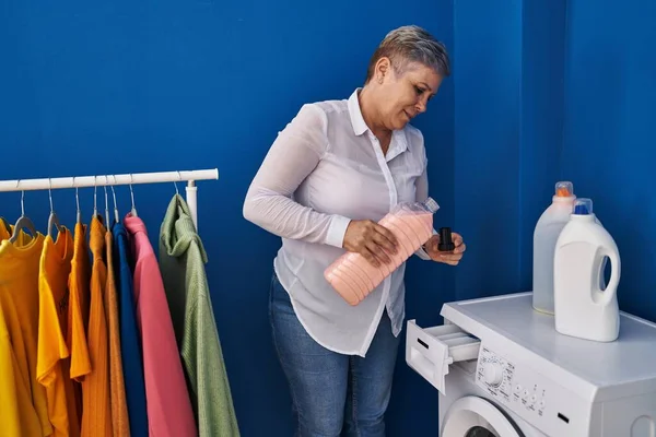 洗濯室で自信を持って洗濯機を注ぐ笑顔中年女性 — ストック写真