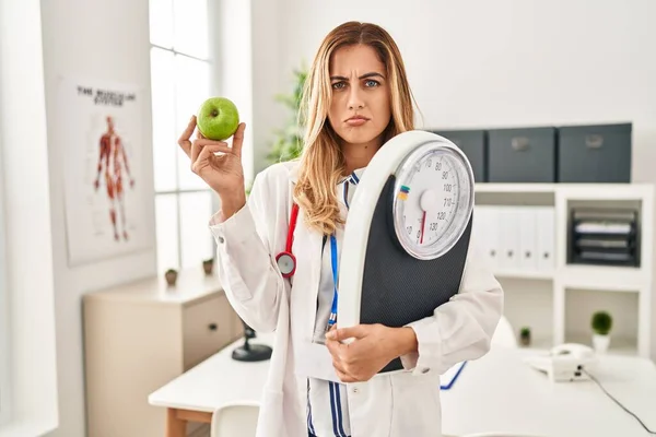計量機と緑のリンゴを保持若いブロンドの医者の女性は落ち込んでおり 苦痛のために心配し 怒って恐れています 悲しい表情 — ストック写真