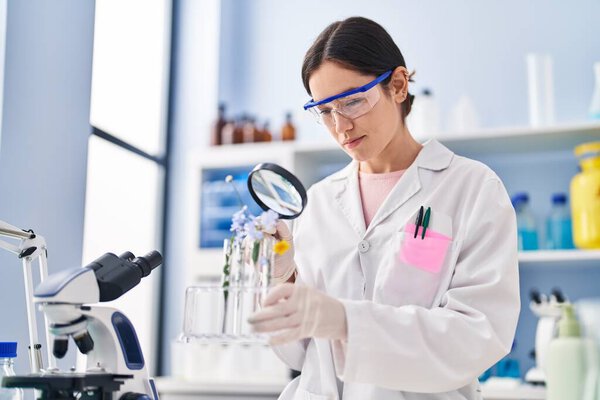 Young woman wearing scientist uniform looking flowers with magnifying glass at laboratory