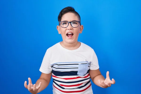 青い背景に立っている若いヒスパニック系の子供は狂気と怒鳴り 積極的な表現と腕を上げて叫んでいます フラストレーションコンセプト — ストック写真