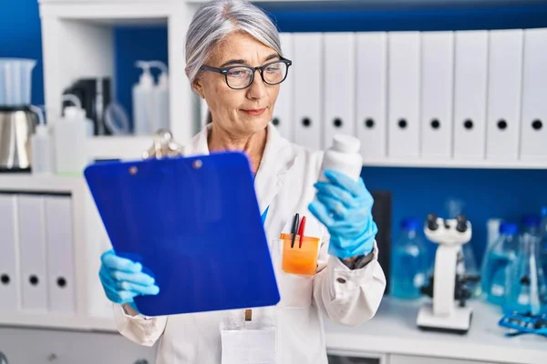 Średniowłosy Kobieta Naukowiec Czyta Dokument Trzymając Butelkę Tabletek Laboratorium — Zdjęcie stockowe