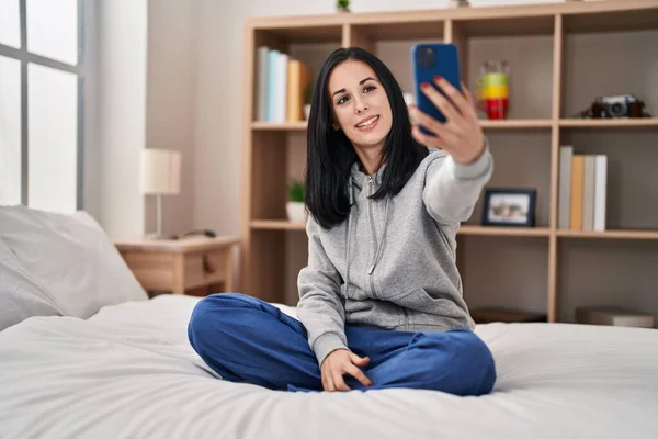 Young caucasian woman make selfie by smartphone sitting on bed at bedroom