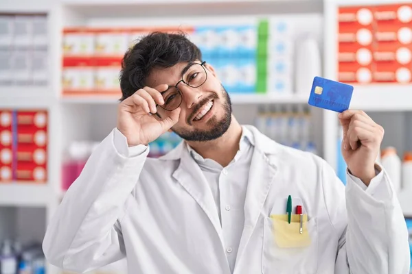 Hombre Hispano Con Barba Trabajando Farmacia Sosteniendo Tarjeta Crédito Sonriendo —  Fotos de Stock