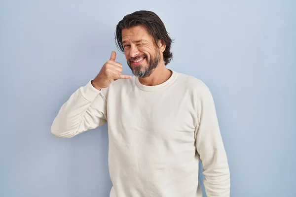 青い背景の上にカジュアルなセーターを着たハンサムな中年の男性は 電話で話すような手や指で電話のジェスチャーをして笑っています コミュニケーションの概念 — ストック写真