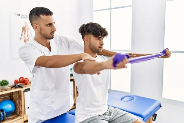 Two Hispanic Men Physiotherapist Patient Having Rehab Session Using Elastic — стоковое фото