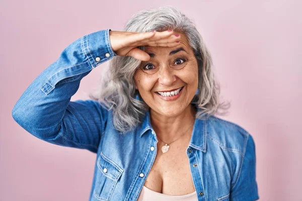 ピンクの背景の上に立っている灰色の髪を持つ中年の女性は非常に幸せと笑顔遠くに手を頭の上に見て 検索の概念 — ストック写真