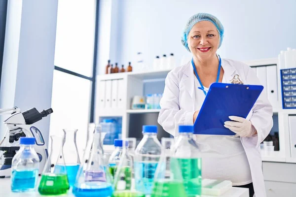Middle Age Blonde Woman Wearing Scientist Uniform Writing Clipboard Laboratory — ストック写真