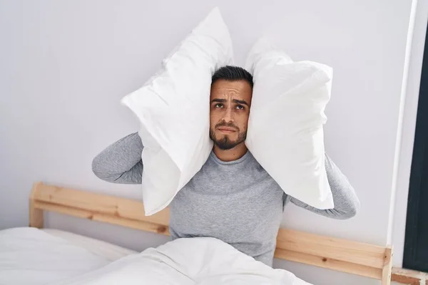 Young hispanic man covering ears for noise at bedroom