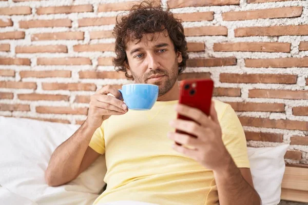 Joven Hispano Usando Smartphone Bebiendo Café Dormitorio —  Fotos de Stock