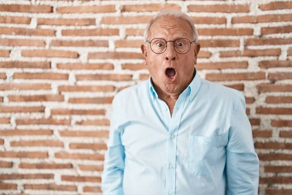 Starszy Mężczyzna Siwymi Włosami Stojący Nad Cegłą Ściana Szoku Twarzy — Zdjęcie stockowe