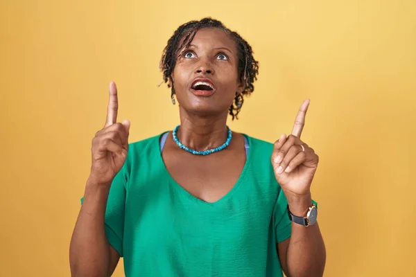 African Woman Dreadlocks Standing Yellow Background Amazed Surprised Looking Pointing — Fotografia de Stock