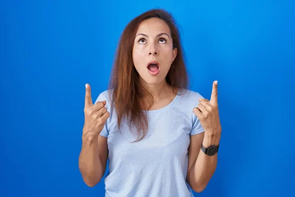Brunette Woman Standing Blue Background Amazed Surprised Looking Pointing Fingers — Stok fotoğraf