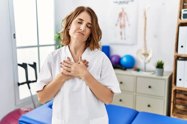 在疼痛康复诊所工作的中年理疗师妇女微笑着双手放在胸前 闭上了眼睛 脸上挂着感激的手势 健康概念 — 图库照片