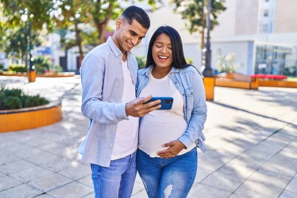 一对年轻的拉丁夫妇在公园里用智能手机期待着孩子的出生 — 图库照片