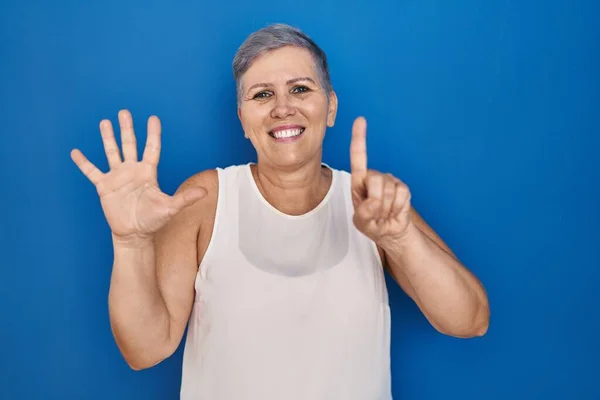 中年的高加索女人站在蓝色的背景上 用六号手指指指指点点 面带微笑 自信而快乐 — 图库照片