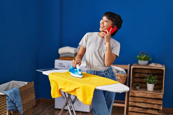 Mujer Joven Hablando Teléfono Inteligente Planchado Ropa Sala Lavandería —  Fotos de Stock