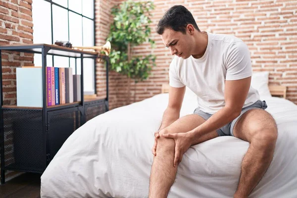 Young Hispanic Man Suffering Knee Injury Sitting Bed Bedroom — Foto de Stock