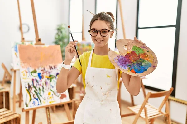可爱的女孩微笑着 自信地在艺术工作室拿着画笔和调色板 — 图库照片
