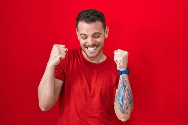 Junger Hispanischer Mann Der Vor Rotem Hintergrund Mit Erhobenen Armen — Stockfoto