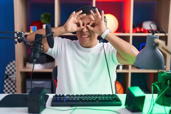 Homem Hispânico Jovem Jogando Videogames Fazendo Gesto Como Binóculos Furando — Fotografia de Stock