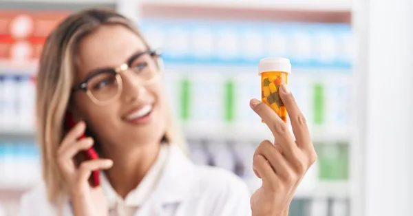 Young Blonde Woman Pharmacist Holding Pills Bottle Talking Smartphone Pharmacy — Stock Photo, Image