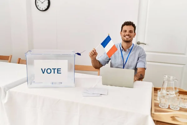 Joven Hispano Sonriendo Confiado Sosteniendo Bandera Francia Trabajando Colegio Electoral —  Fotos de Stock