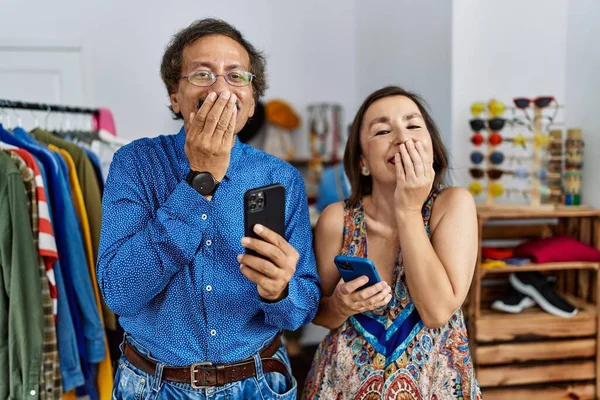 中世異人種間のカップルで小売店で使用スマートフォン笑いと恥ずかしがり屋クスクスカバー口で手 ゴシップやスキャンダルの概念 — ストック写真
