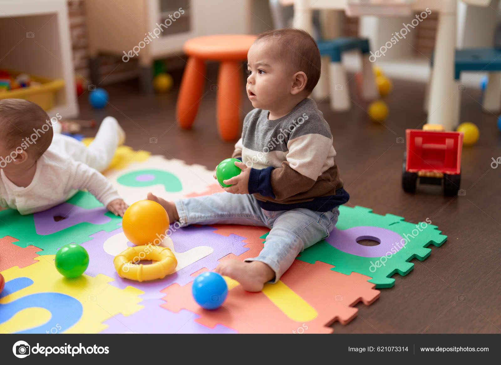 Adorável bebê caucasiano brincando com bolas sentadas no chão no jardim de  infância