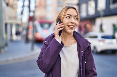 Gülümseyen genç bir kadın caddedeki akıllı telefondan konuşuyor.