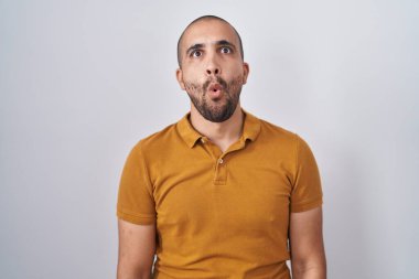 Hispanic man with beard standing over white background making fish face with lips, crazy and comical gesture. funny expression. 