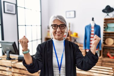 Orta yaşlı, gri saçlı, mağaza müdürü olarak çalışan çok mutlu ve heyecanlı bir kadın. Kolları havada, gülümseyen ve başarı için bağıran bir jest yapıyor. kutlama konsepti. 