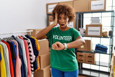 Young african american woman wearing volunteer t shirt at donations stand looking at the watch time worried, afraid of getting late 
