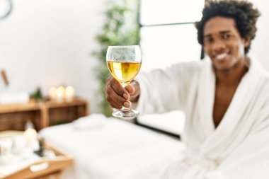 Genç Afro-Amerikan adam kendine güvenen bir şekilde gülümsüyor güzellik merkezinde şampanya içiyor.