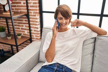 Evdeki kanepede oturmuş akıllı telefondan konuşan genç, güzel İspanyol kadın.