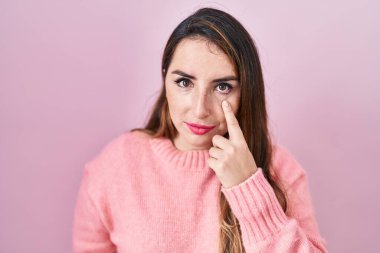 Pembe arka planda duran genç İspanyol kadın senin jestini ve şüpheli ifadesini izleyerek göze işaret ediyor. 