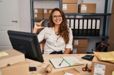 Küçük işletme şirketinde çalışan Latin kökenli genç bir kadın gülümsüyor ve el hareketleriyle el hareketi yapıyor. Parmakları ve kamerasıyla küçük boy işareti yapıyor. ölçüm kavramı. 